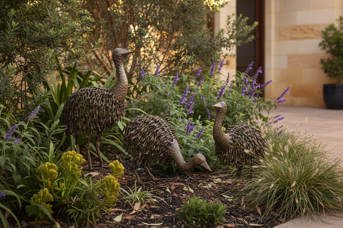 Set of 3 rustic metal emu chick garden statues in black rust finish displayed in an Australian garden bed with native plants and warm natural light