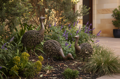 Set of 3 rustic metal emu chick garden statues in black rust finish displayed in an Australian garden bed with native plants and warm natural light